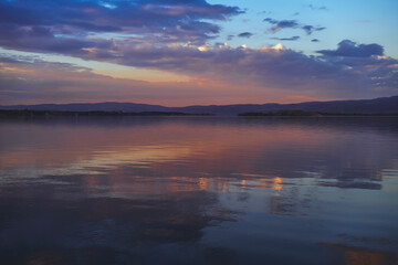 Fototapeta premium Sunset landscape. Lake water surface with reflection of clouds in the water