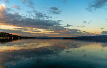 Sunset landscape. Lake water surface with reflection of clouds in the water