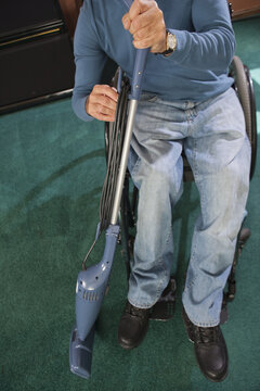Man with spinal cord injury in a wheelchair rewinding power cord on vacuum cleaner