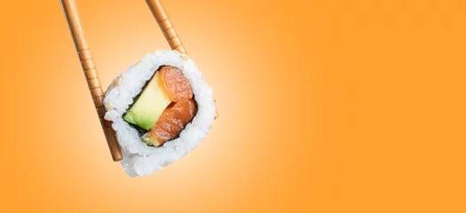 Gordijnen sushi roll in chopsticks with copy space © Miquel