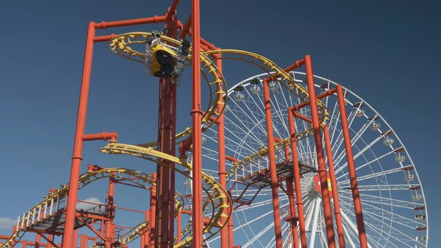 Spiral roller coaster ride and ferris wheel against blue sky in amusement park