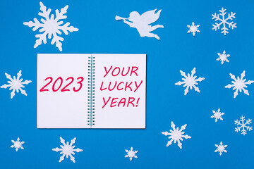 An open notepad diary with the Text 2023 and YOUR LUCKY YEAR on a blue background with Christmas snowflakes