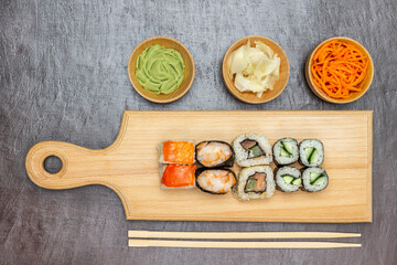 Sushi on a cutting board. Chopsticks on the table. Wasabi, pickled ginger and carrots in bowls.