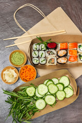 Fototapeta na wymiar Takeaway food. Rosemary sprigs and sliced cucumbers, sushi in paper plates. Seasonings in bowls.
