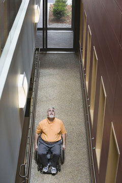 High angle view of a middle-aged man with Muscular Dystrophy sitting in a wheelchair in a library