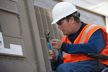 Facilities engineer in a wheelchair opening inspection plate of commercial air conditioning system