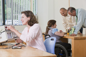 Student connecting function generator while professor is demonstrating circuit board in background