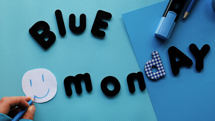 Chica dibujando una cara sonriente en un fondo azul con letras de Blue Monday y material de...