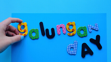 Chica colocando una letra de galungan day fiesta balinesa en un fondo azul