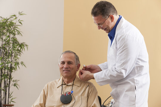 Audiologist inserting behind-the-ear hearing aid into a patient's ear during programming