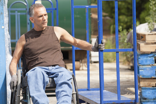 Loading dock worker with spinal cord injury in a wheelchair moving a hand truck