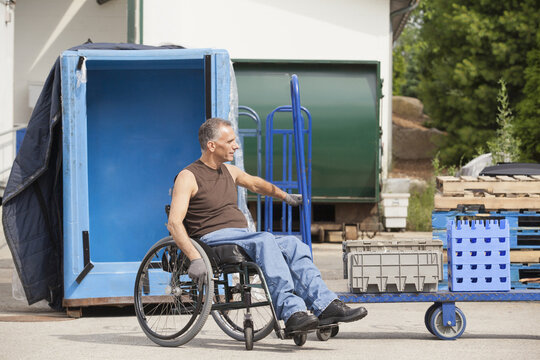 Loading dock worker with spinal cord injury in a wheelchair moving a hand truck