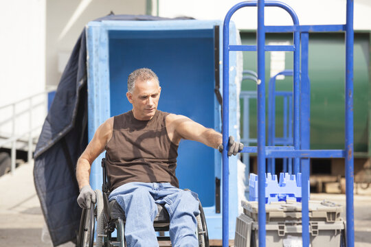 Loading dock worker with spinal cord injury in a wheelchair moving a hand truck