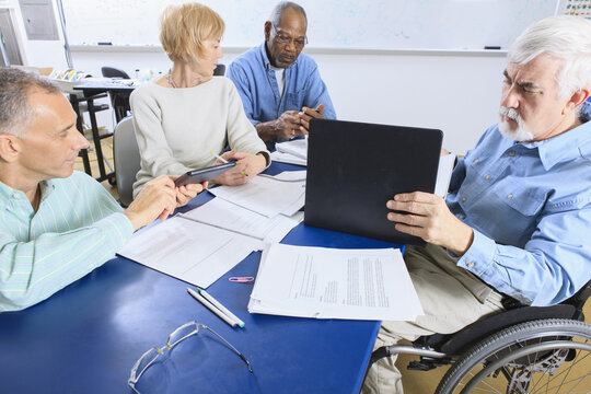 Professors in a faculty meeting, one in a wheelchair with Muscular Dystrophy