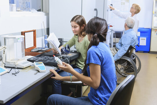 Engineering students working on a chemical analysis kit with professors in background, one with Muscular Dystrophy