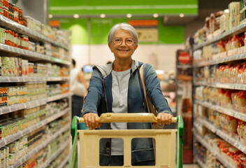 Retired senior woman pushing shopping trolley in supermarket shopping for groceries being careful...