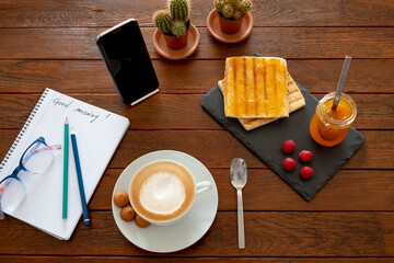 Breakfast time with hot cappuccino and toasted bread with jam. Mobile phone for breaking news, good...