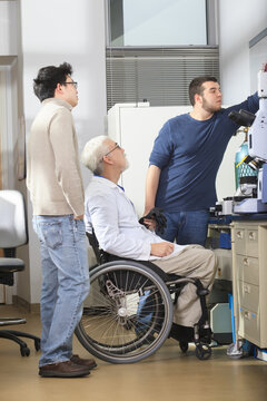 Professor with muscular dystrophy working with engineering students adjusting camera on x-ray fluorescence analyzer in a laboratory