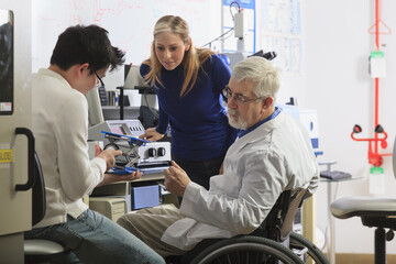 Professor with muscular dystrophy working with engineering students setting up adjustable stage at chemical analysis instrument in a laboratory
