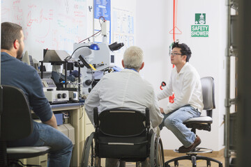 Professor with muscular dystrophy and engineering students reviewing procedures for x-ray fluorescence experiment in a laboratory