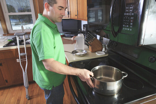 Man after anterior cruciate ligament (ACL) surgery with crutches cooking in the kitchen