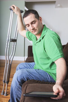 Man after anterior cruciate ligament (ACL) surgery with crutches and an digital tablet at home