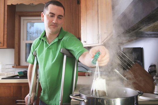 Man after anterior cruciate ligament (ACL) surgery with crutches making tea in the kitchen