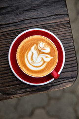 A cup of cappuccino with rose on top on wooden table