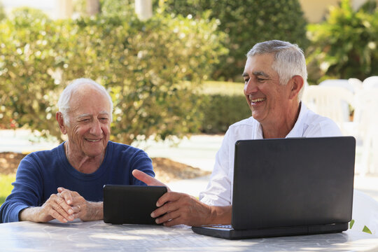 Senior man smiling showing a digital tablet to his father, who is visually impaired