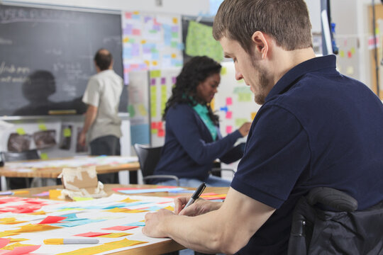 Student preparing ideation notes in an engineering fabrication laboratory, one man with spinal cord injury and other one with Aspergers