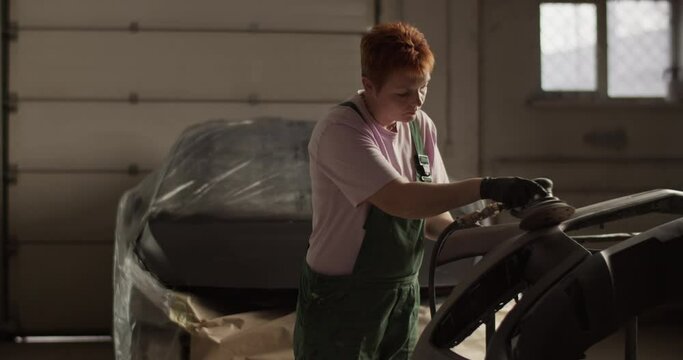 Female painter preparing car bumper for painting