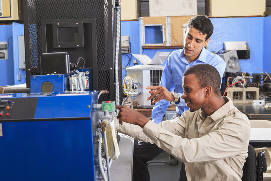 Student in wheelchair studying natural gas injector system on furnace with his classmate in HVAC classroom