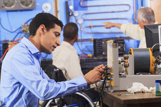 Student setting up generator experiment while instructor discusses HVAC system to student in wheelchair