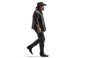 Full length profile shot of a man in leather clothes and a black cowboy hat walking