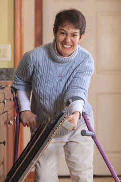 Woman With Cerebral Palsy Using Crutches And Opening Her Oven In Her Kitchen