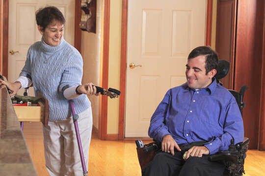 Woman with Cerebral Palsy using crutches and giving a can opener to her husband in a wheelchair with Cerebral Palsy