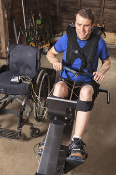 Man with spinal cord injury using his rowing machine with a muscle stimulator attached