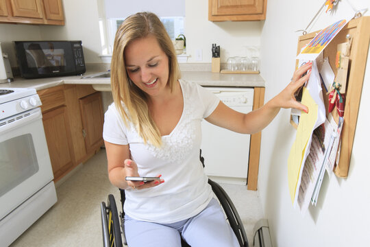 Woman with spinal cord injury in her accessible kitchen looking at her mobile phone