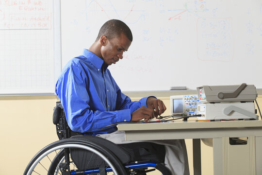 Engineering student sitting in a wheelchair preparing lab experiment with oscilloscope and electronic prototyping breadboard