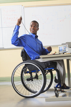 Engineering student sitting in a wheelchair preparing lab experiment with oscilloscope and electronic prototyping breadboard