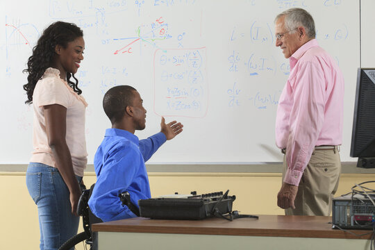 Electronics professor discussing equation on whiteboard to engineering students, one in wheelchair