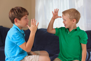 Boys with hearing impairments signing 'mom, dad or parents' in American sign language on their couch