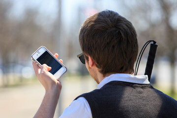 Young blind man with cane using assistive technology in his neighborhood