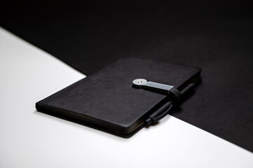 black organizer or notebook with pen on two-color black and white background, mockup, copy space