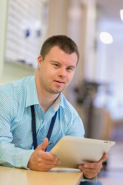Young man with Down Syndrome working as a hospital aid with his tablet