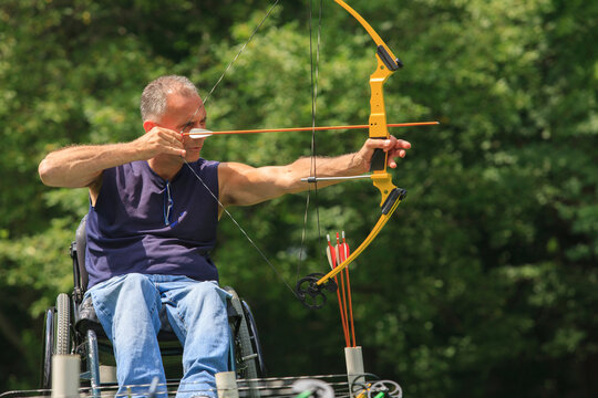 Man with spinal cord injury in wheelchair aiming his bow and arrow for archery practice