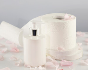 Roll of toilet paper with cosmetic dispenser bottle on light background with rose petals. White toilet tissue, Hygiene product. Restroom soft touch toilet paper. Soft focus style image
