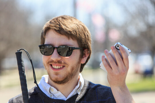 Young blind man with cane using assistive technology in his neighborhood