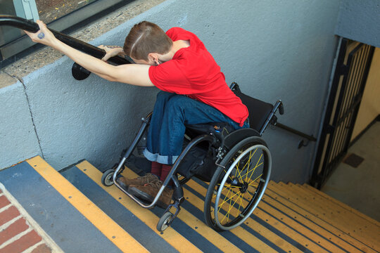 Trendy man with a spinal cord injury in wheelchair going down subway stairs backwards