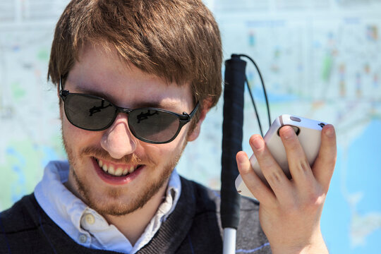 Young blind man with cane using assistive technology